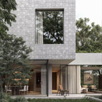 Modern home exterior featuring natural stone facade, large window, and minimalist design with lush greenery.